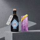 The Illusionist Masquerade Alcohol-Free Bottle Next to Pink Cocktail in a Glass